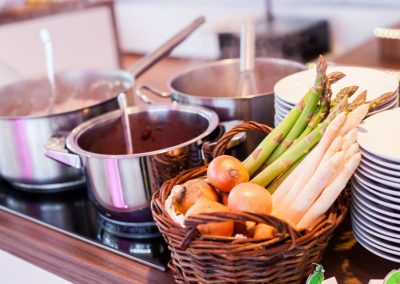 Töpfe auf dem Herd und Korb mit Spargel und Zwiebeln